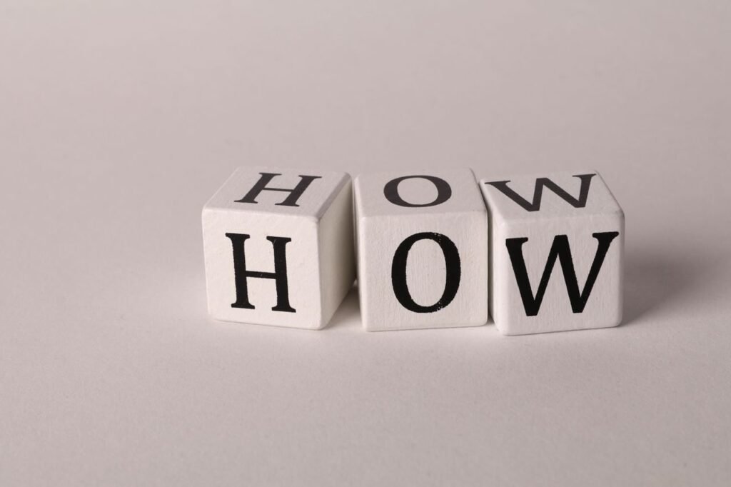 Close-up of white wooden cubes with the letters 'H', 'O', and 'W' arranged on a neutral background.