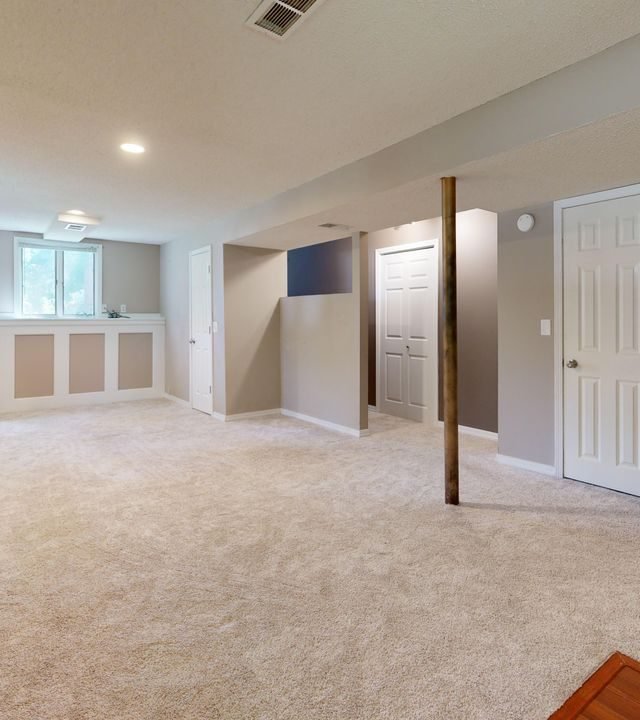 Bright and clean modern basement with carpet flooring and recessed lighting.